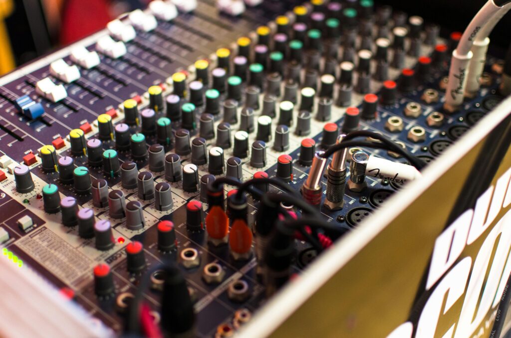 Close-up of a professional audio mixer with colorful knobs and cables in a studio setting.
